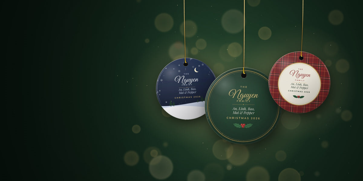 Three personalized Kindred Bough ceramic family ornaments hanging on gold strings against a deep evergreen background